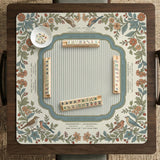 Square mahjong mat with a cream background, blue birds, sage leaves, terracotta flowers, and a decorative botanical border with printed rules text.