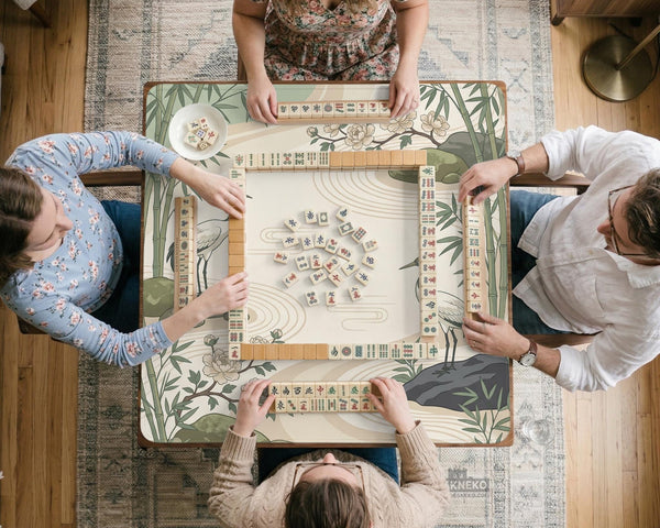 Square mahjong mat with a cream background, sage green cranes, bamboo leaves, peony branches, stones, and thin linework.