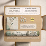 Square mahjong mat with a cream background, sage green cranes, bamboo leaves, peony branches, stones, and thin linework.