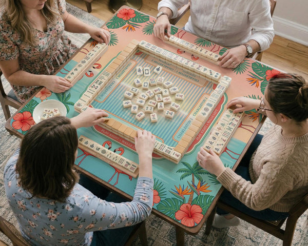 Pink mahjong mat with flamingos, palm leaves, hibiscus flowers, and aqua tropical background.