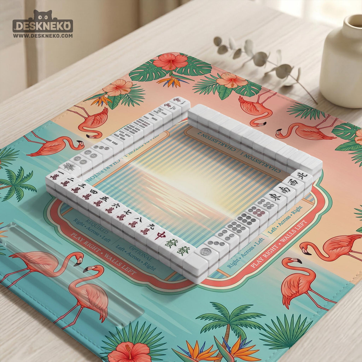 A square mahjong mat with flamingos, hibiscus flowers, palm leaves, and aqua water accents on a coral background with a scalloped edge.