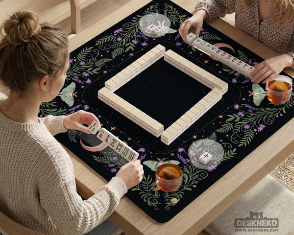 Black mahjong table mat with luna moths, purple flowers, soft green leaves, copper moons, and small star details.