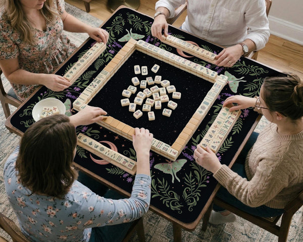 Black mahjong table mat with luna moths, purple flowers, soft green leaves, copper moons, and small star details.