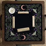 Black mahjong table mat with luna moths, purple flowers, soft green leaves, copper moons, and small star details.