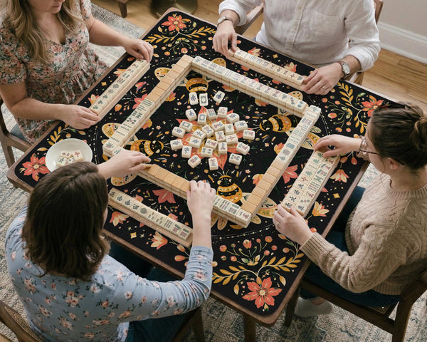 Black mahjong mat with a symmetrical botanical design, coral flowers, golden leaves, and small bees.