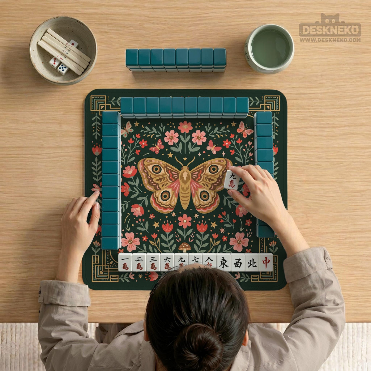 Dark green square mahjong mat with floral branches, small red blossoms, gold line details, and a large moth in the center.