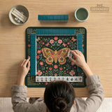 Dark green square mahjong mat with floral branches, small red blossoms, gold line details, and a large moth in the center.