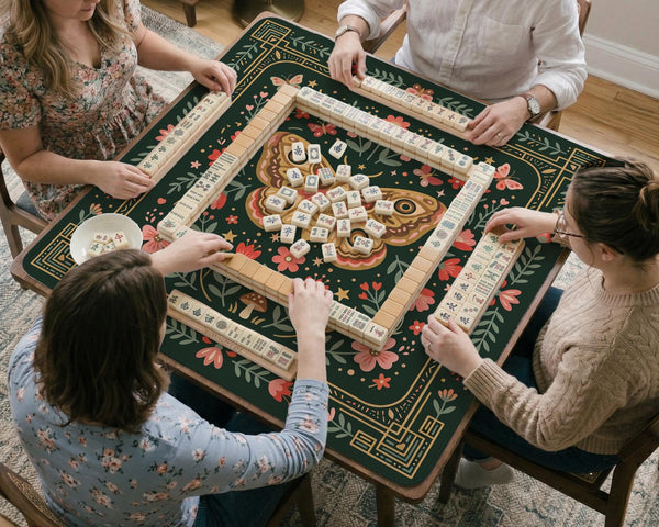 Dark green square mahjong mat with floral branches, small red blossoms, gold line details, and a large moth in the center.