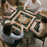 Dark green square mahjong mat with floral branches, small red blossoms, gold line details, and a large moth in the center.