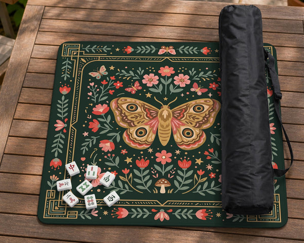 Dark green square mahjong mat with floral branches, small red blossoms, gold line details, and a large moth in the center.