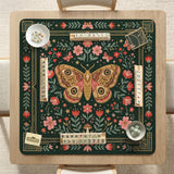 Dark green square mahjong mat with floral branches, small red blossoms, gold line details, and a large moth in the center.