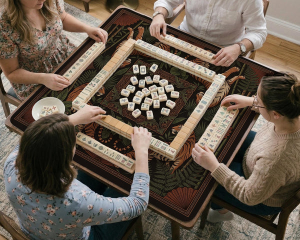 Black square mahjong mat with mirrored tiger faces, bamboo, dark tropical leaves, ornate border details, and orange accents.