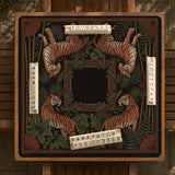 Black square mahjong mat with mirrored tiger faces, bamboo, dark tropical leaves, ornate border details, and orange accents.