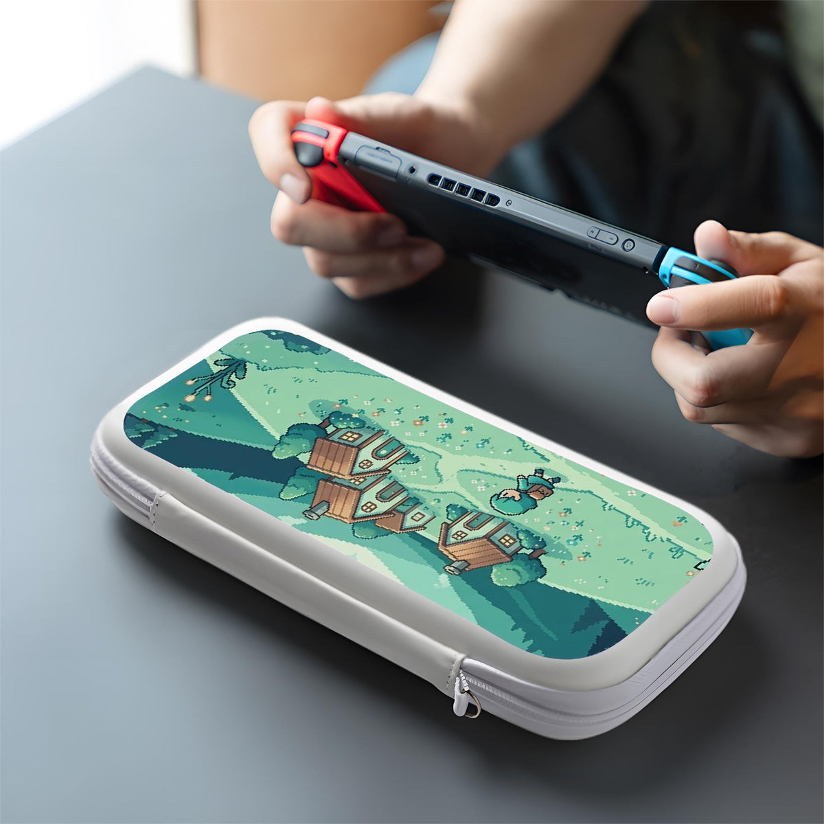 Teal carrying case with a pixel-style village scene, small houses, layered mountains, flowers, and a retro game-inspired landscape design.