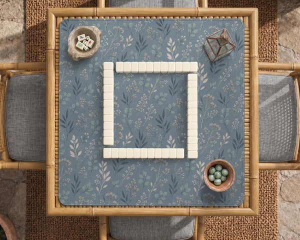 Blue mahjong mat with a botanical floral pattern, pale leaves, and delicate stems on a dusty blue background.
