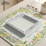 Square yellow mahjong mat with a citrus garden border, green vines, pink blossoms, aqua accents, and a plain center play area.