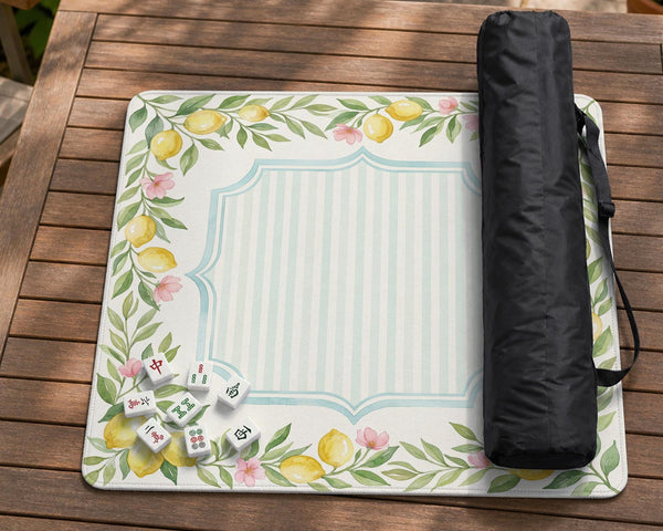 Square yellow mahjong mat with a citrus garden border, green vines, pink blossoms, aqua accents, and a plain center play area.
