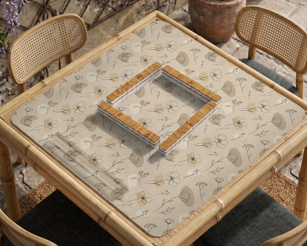 Neutral floral mahjong mat with delicate botanical line art and a scalloped edge on a cream background.