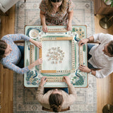 Teal square mahjong mat with peacock feathers, soft floral pattern, tassel details, and printed rule guide text in the center.