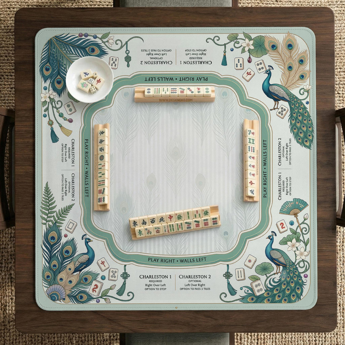 Teal square mahjong mat with peacock feathers, soft floral pattern, tassel details, and printed rule guide text in the center.