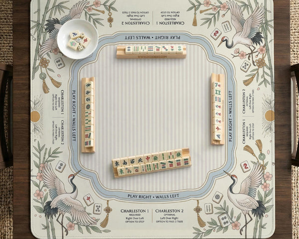 Beige square mahjong mat with a sage border, crane birds, bamboo, flowers, tile icons, and printed rules around a clean center play area.
