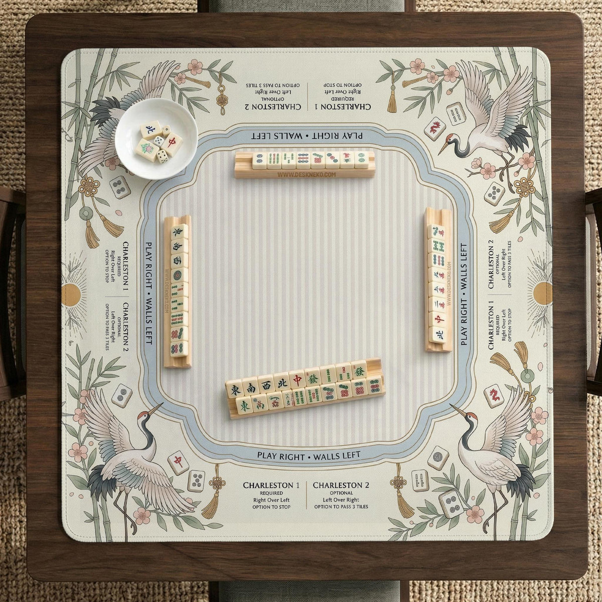 Beige square mahjong mat with a sage border, crane birds, bamboo, flowers, tile icons, and printed rules around a clean center play area.
