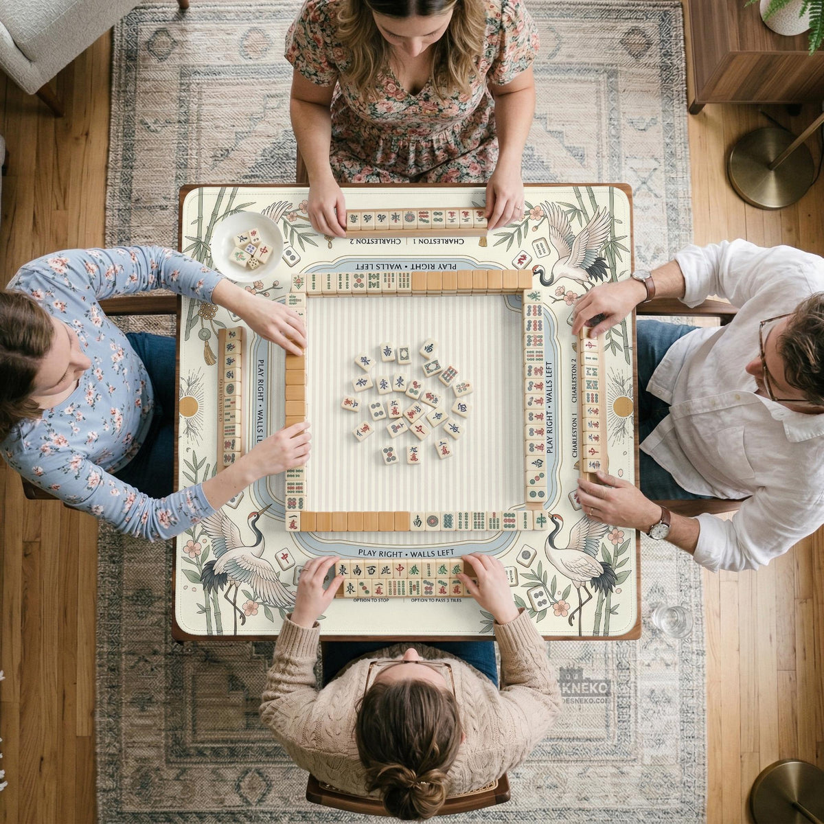 Beige square mahjong mat with a sage border, crane birds, bamboo, flowers, tile icons, and printed rules around a clean center play area.