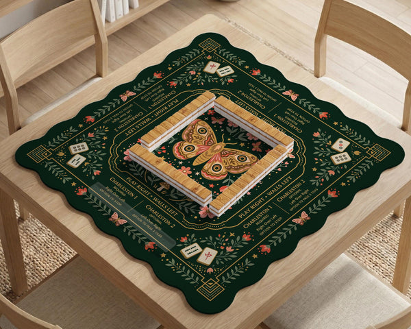 Dark botanical mahjong table mat with a floral border, large moth and butterfly design in the center, gold corner frame, and printed rules layout around the edge.