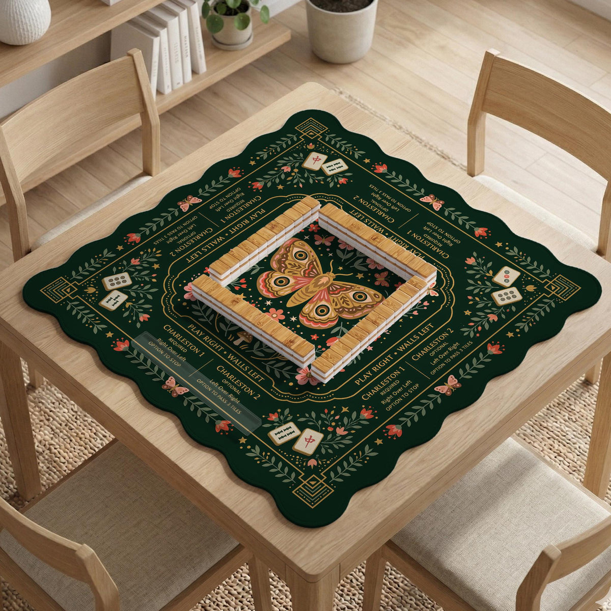 Dark botanical mahjong table mat with a floral border, large moth and butterfly design in the center, gold corner frame, and printed rules layout around the edge.