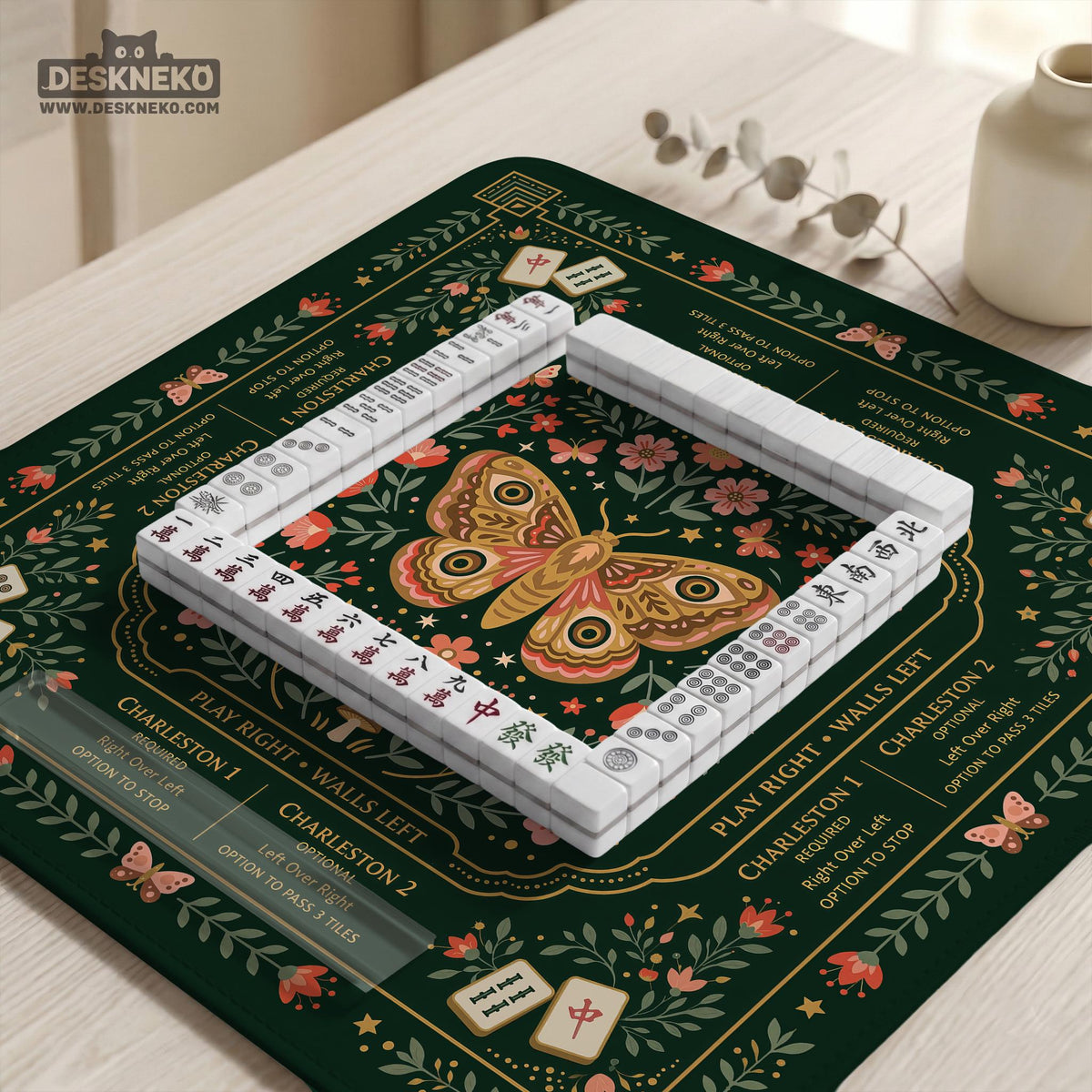 Dark botanical mahjong table mat with a floral border, large moth and butterfly design in the center, gold corner frame, and printed rules layout around the edge.