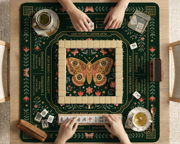 Dark botanical mahjong table mat with a floral border, large moth and butterfly design in the center, gold corner frame, and printed rules layout around the edge.