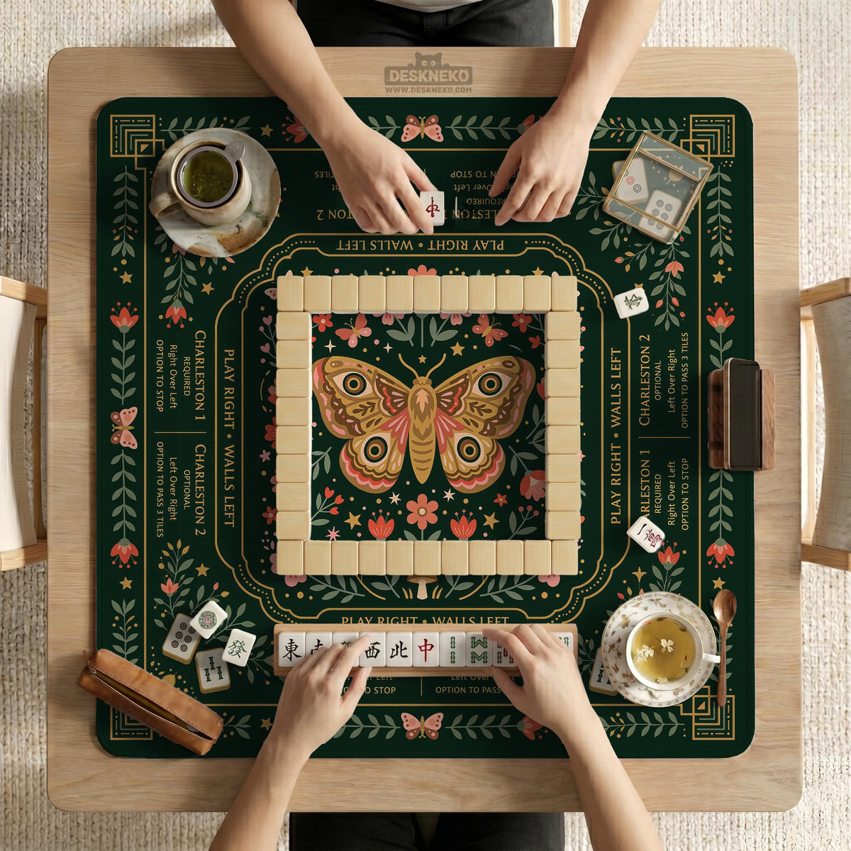 Dark botanical mahjong table mat with a floral border, large moth and butterfly design in the center, gold corner frame, and printed rules layout around the edge.