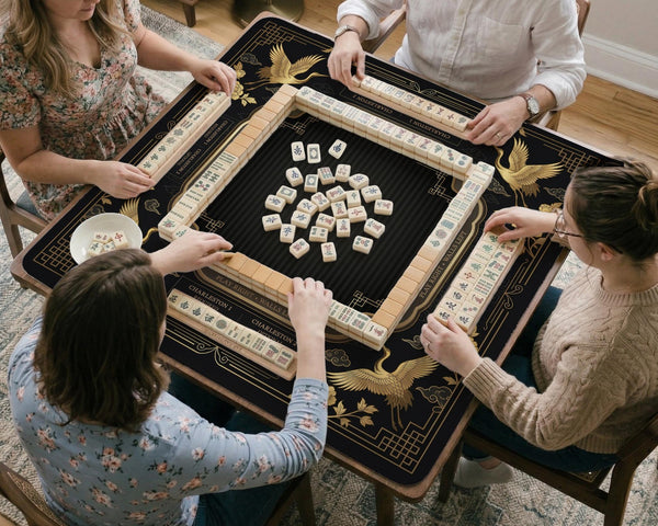 Black and gold square mahjong mat with an art deco crane and floral border, rule reminders around the edges, and a blank center area.