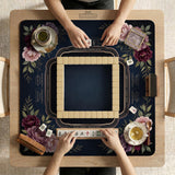 Burgundy mahjong mat with a floral border, gold botanical details, and printed American Mahjong rules on a dark background.