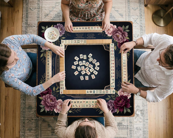 Burgundy mahjong mat with a floral border, gold botanical details, and printed American Mahjong rules on a dark background.