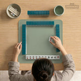 A square sage green mahjong mat with scalloped edges on a plain background.