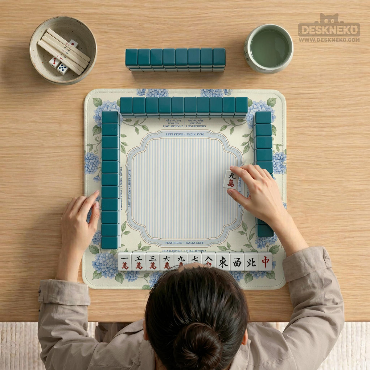 A square mahjong mat with blue hydrangea flowers, green vines, a cream background, a striped center, and printed rules around the border.