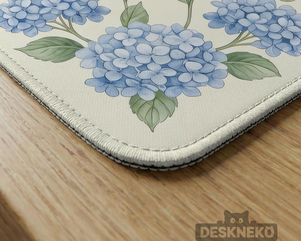 A square mahjong mat with blue hydrangea flowers, green vines, a cream background, a striped center, and printed rules around the border.