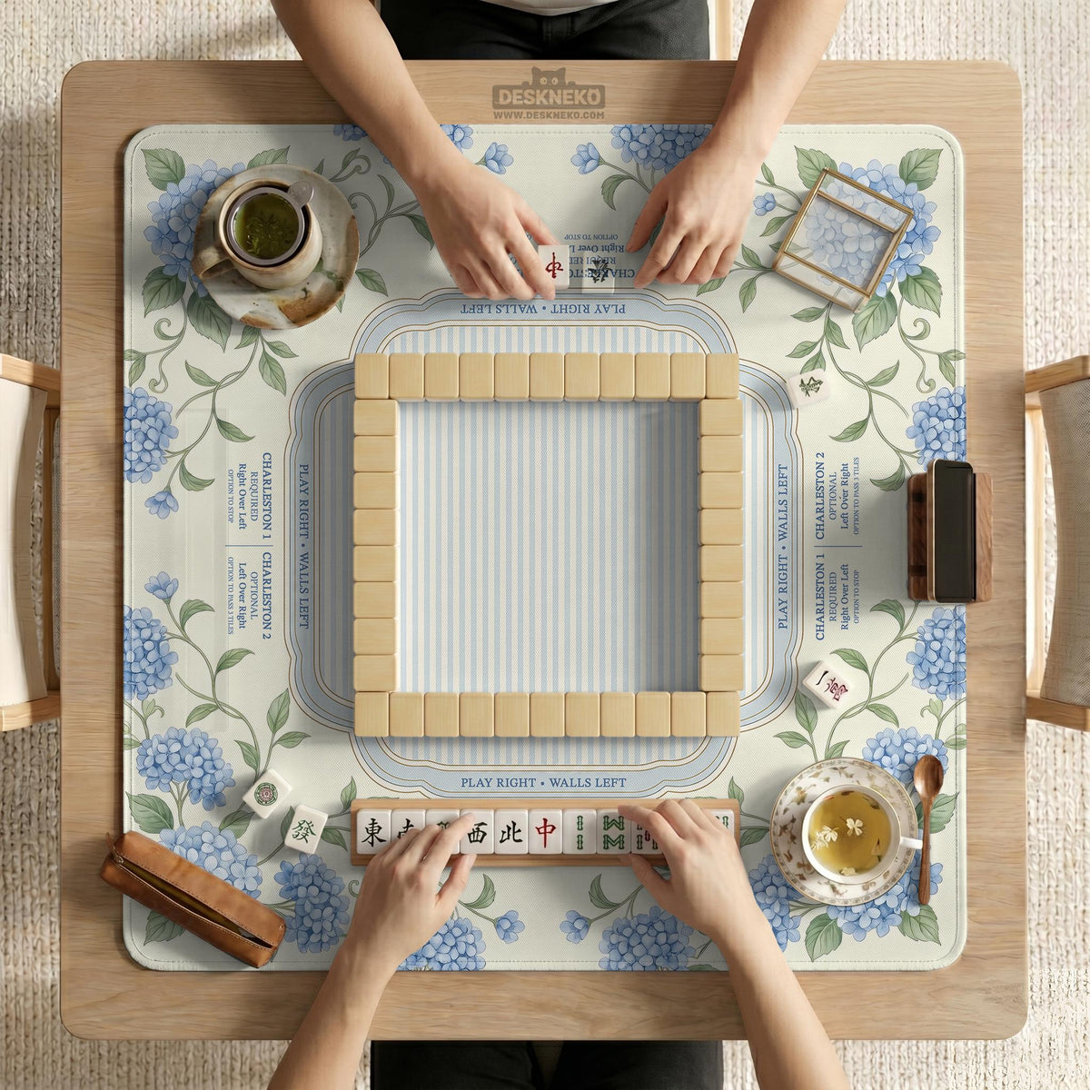 A square mahjong mat with blue hydrangea flowers, green vines, a cream background, a striped center, and printed rules around the border.