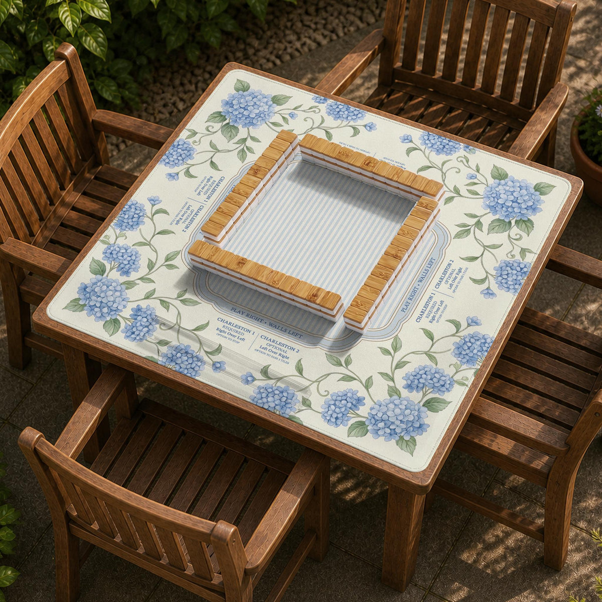 A square mahjong mat with blue hydrangea flowers, green vines, a cream background, a striped center, and printed rules around the border.