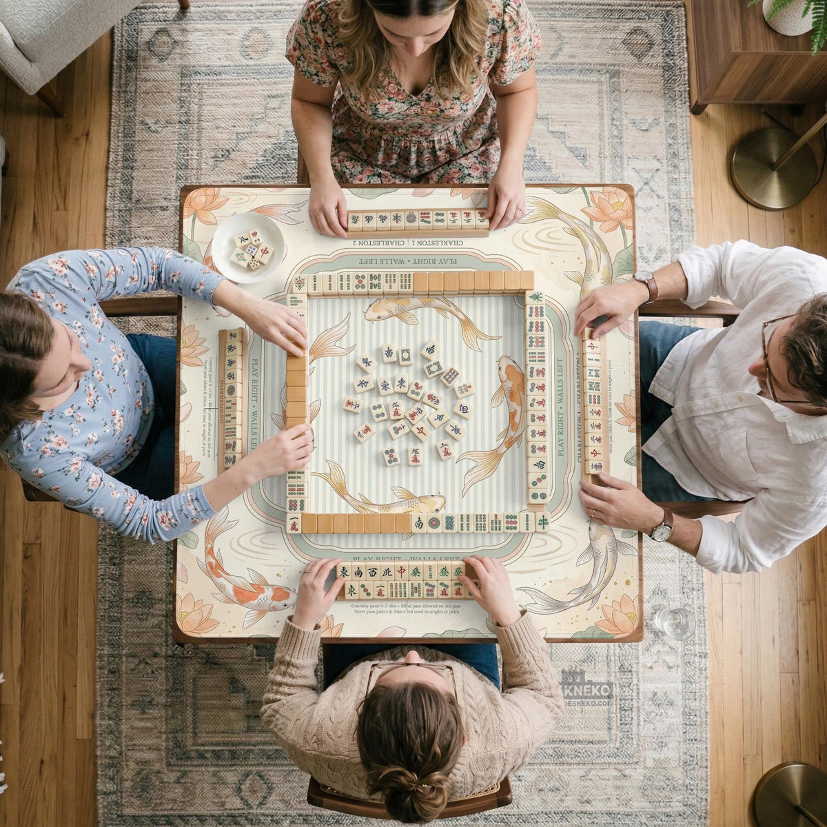 Sage and cream mahjong mat with a koi fish pond pattern, lotus blooms, water ripples, and printed instructions around the border. One version has a scalloped edge.