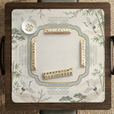 Sage green scalloped mahjong mat with bamboo, crane, and blossom illustration and printed rules around the border.