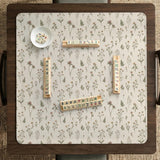 Cream mahjong mat with a floral pattern of small wildflowers and sage leaves, shown with a scalloped edge on a light neutral background.