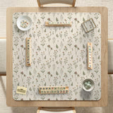 Cream mahjong mat with a floral pattern of small wildflowers and sage leaves, shown with a scalloped edge on a light neutral background.