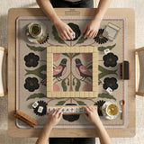Beige mahjong mat with a botanical floral bird design, blush flowers, olive green leaves, black flower accents, and a warm linen-style background. Scalloped edge option shown.