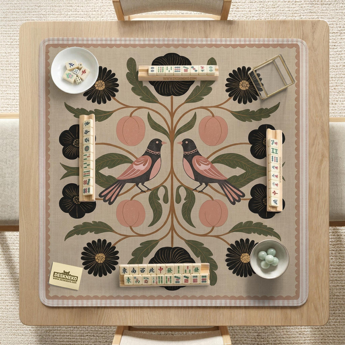 Beige mahjong mat with a botanical floral bird design, blush flowers, olive green leaves, black flower accents, and a warm linen-style background. Scalloped edge option shown.