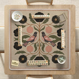 Beige mahjong mat with a botanical floral bird design, blush flowers, olive green leaves, black flower accents, and a warm linen-style background. Scalloped edge option shown.
