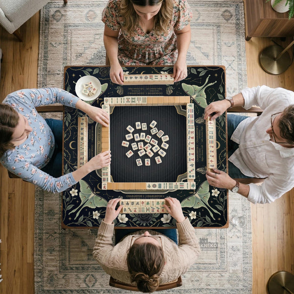 A dark floral mahjong mat with a scalloped edge, moth and flower artwork, and an American Mahjong rules layout on a dark background.