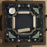A dark floral mahjong mat with a scalloped edge, moth and flower artwork, and an American Mahjong rules layout on a dark background.