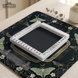 A dark floral mahjong mat with a scalloped edge, moth and flower artwork, and an American Mahjong rules layout on a dark background.